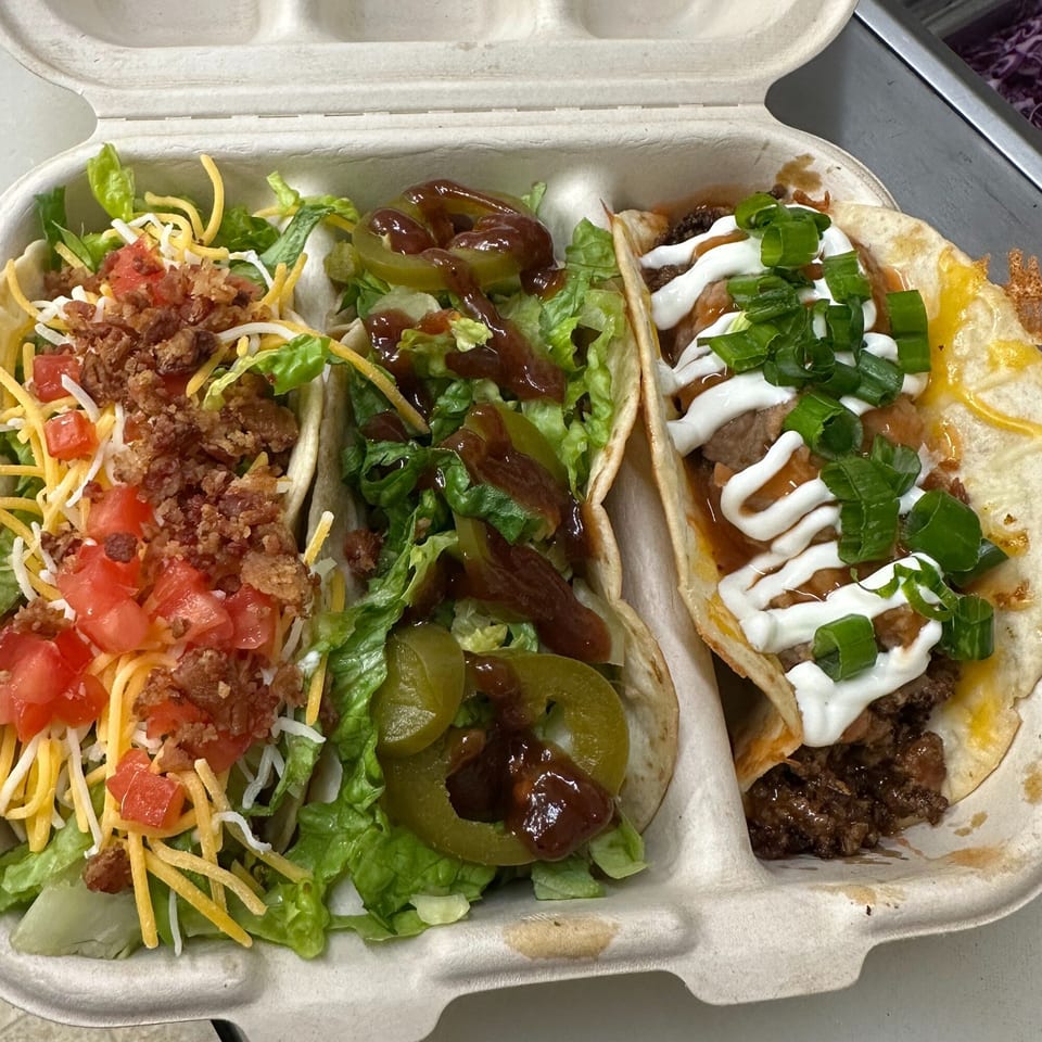 Three Krazy Taco 937 tacos in a takeout container, topped with various ingredients.