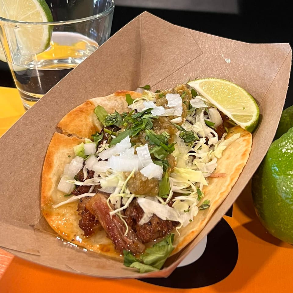 A Krazy Taco 937 taco with meat, salsa, onions, and cilantro, served with a lime wedge.