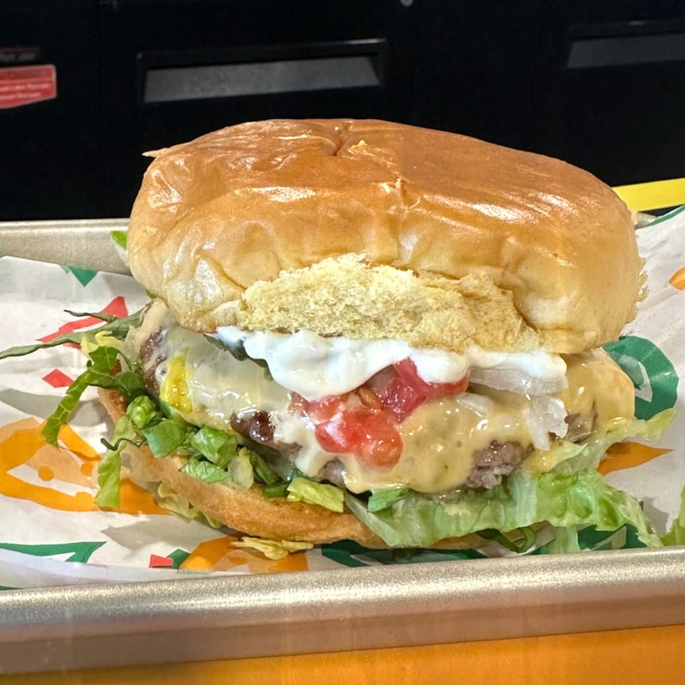 A Krazy Taco 937 burger with lettuce, cheese, tomatoes, onions, and sour cream on a tray.