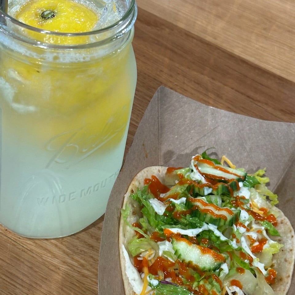 A Krazy Taco 937 taco with lettuce, cheese, and sauce next to a mason jar of lemonade.