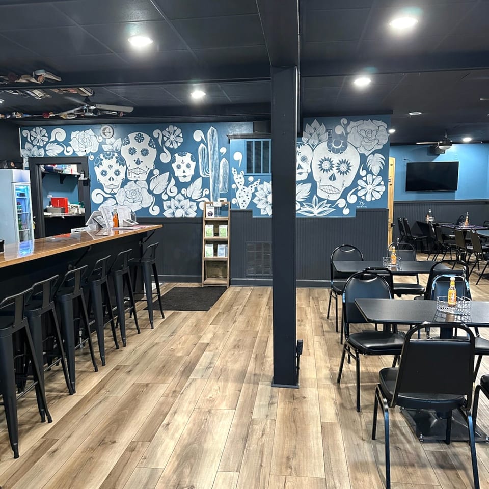 Interior of Krazy Taco 937 with a bar, tables, and a blue wall mural with sugar skulls.