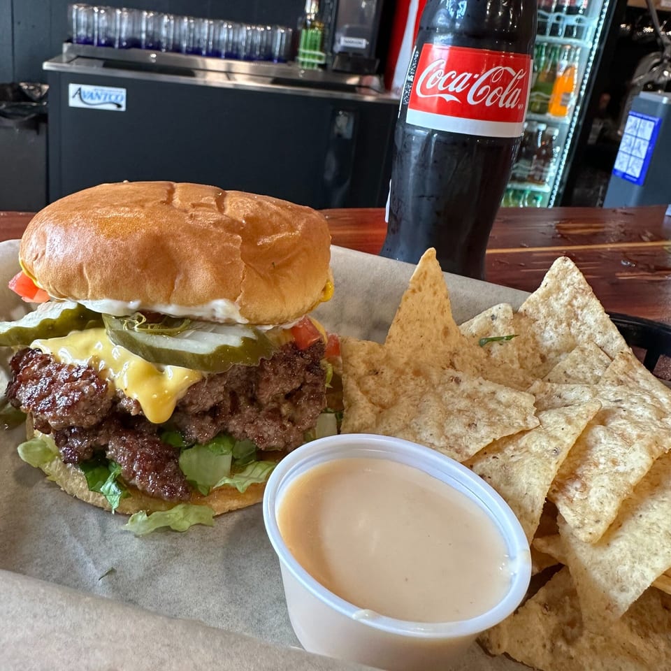 A Krazy Taco 937 burger with cheese, pickles, and lettuce, served with tortilla chips and dip.
