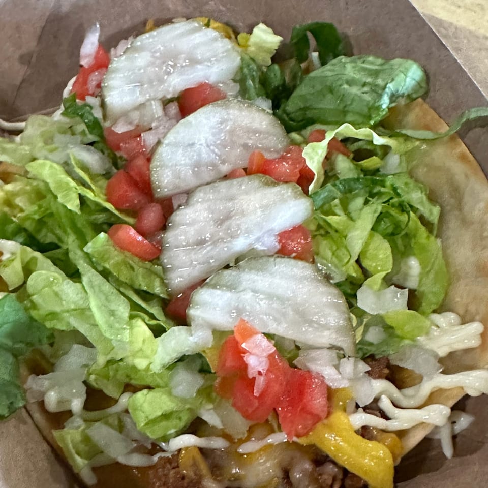 Krazy Taco 937 taco with ground beef, cheese, lettuce, tomatoes, and pickles in a shell.