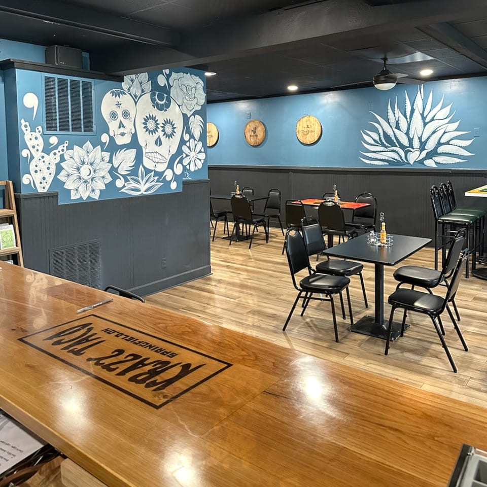 Interior of Krazy Taco 937 with blue walls, murals, wooden floors, and black tables and chairs.